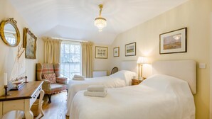 Habitación de hotel con dos camas, un escritorio con silla, una lámpara y cuadros en las paredes.