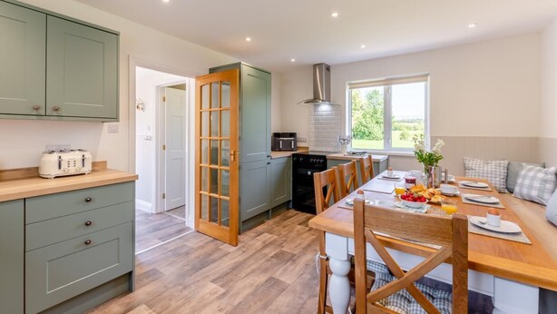 A modern kitchen with a dining area, wooden flooring, and a view of the outdoors. - 4 Bed in Ireby (oc-p34997) (Ireby)