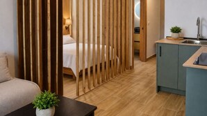 Ein modernes Hotelzimmer mit einem Bett, einem kleinen Tisch mit einer Pflanze, einer Küchenzeile und einem Holztrenner.