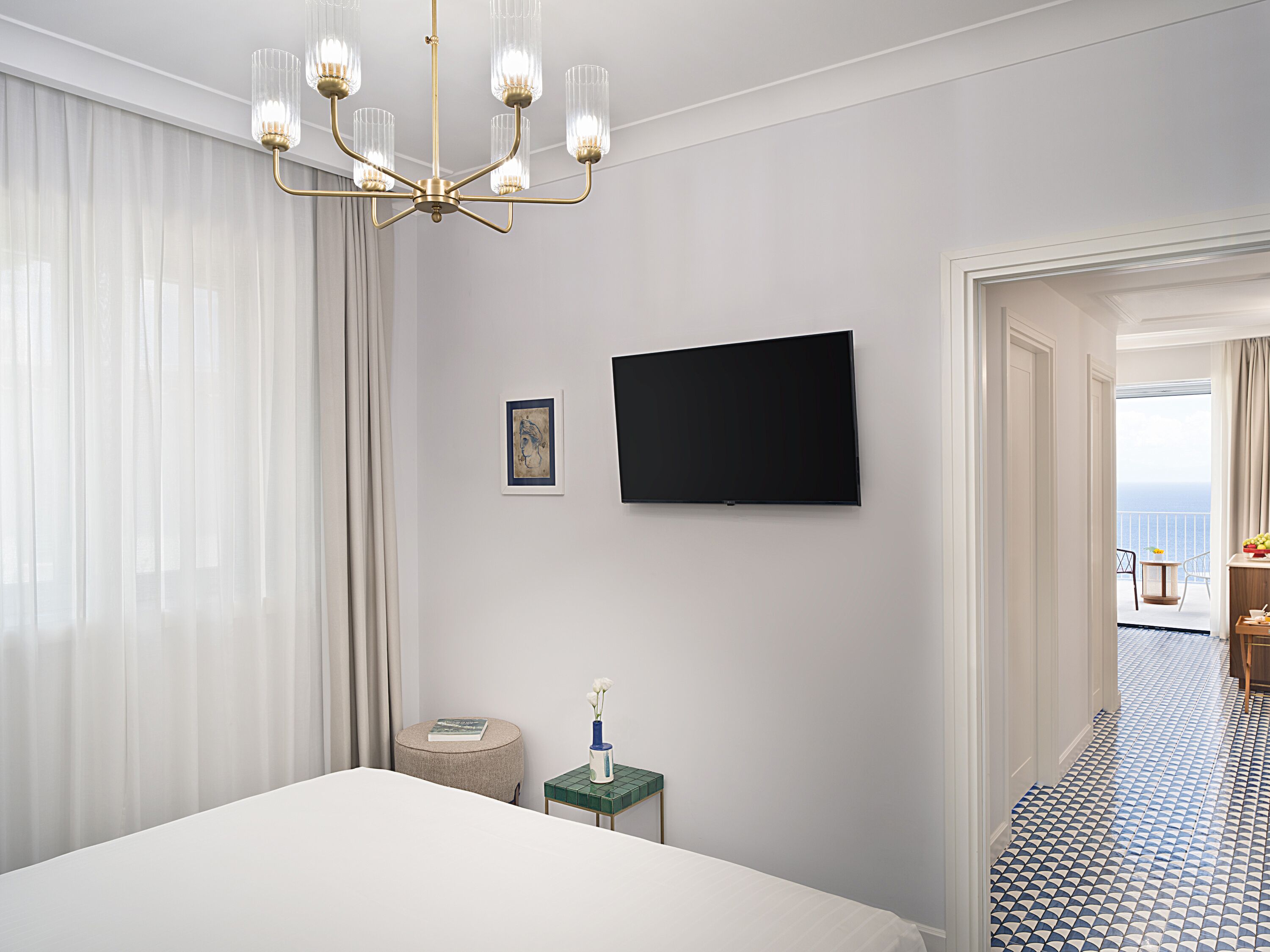 Habitación de hotel con cama, televisión, una mesita con un florero y vista al mar desde un balcón.
