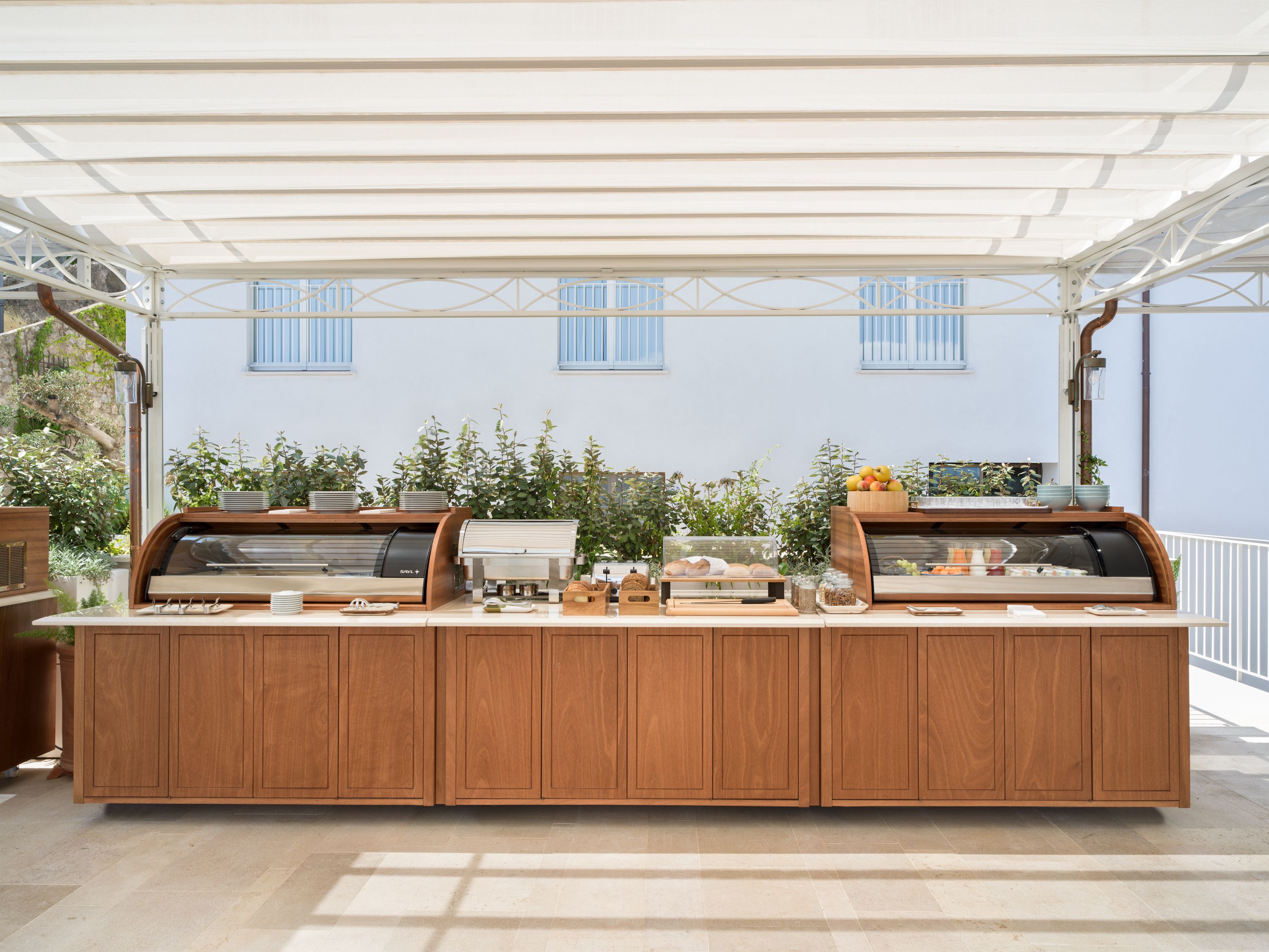 An outdoor buffet setup with a wooden counter, various food items, and a white canopy.