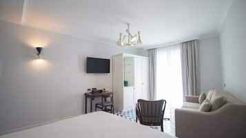 A hotel room with a bed, a desk, a chair, a sofa, a flat-screen TV, a chandelier, and a door leading to a bathroom.