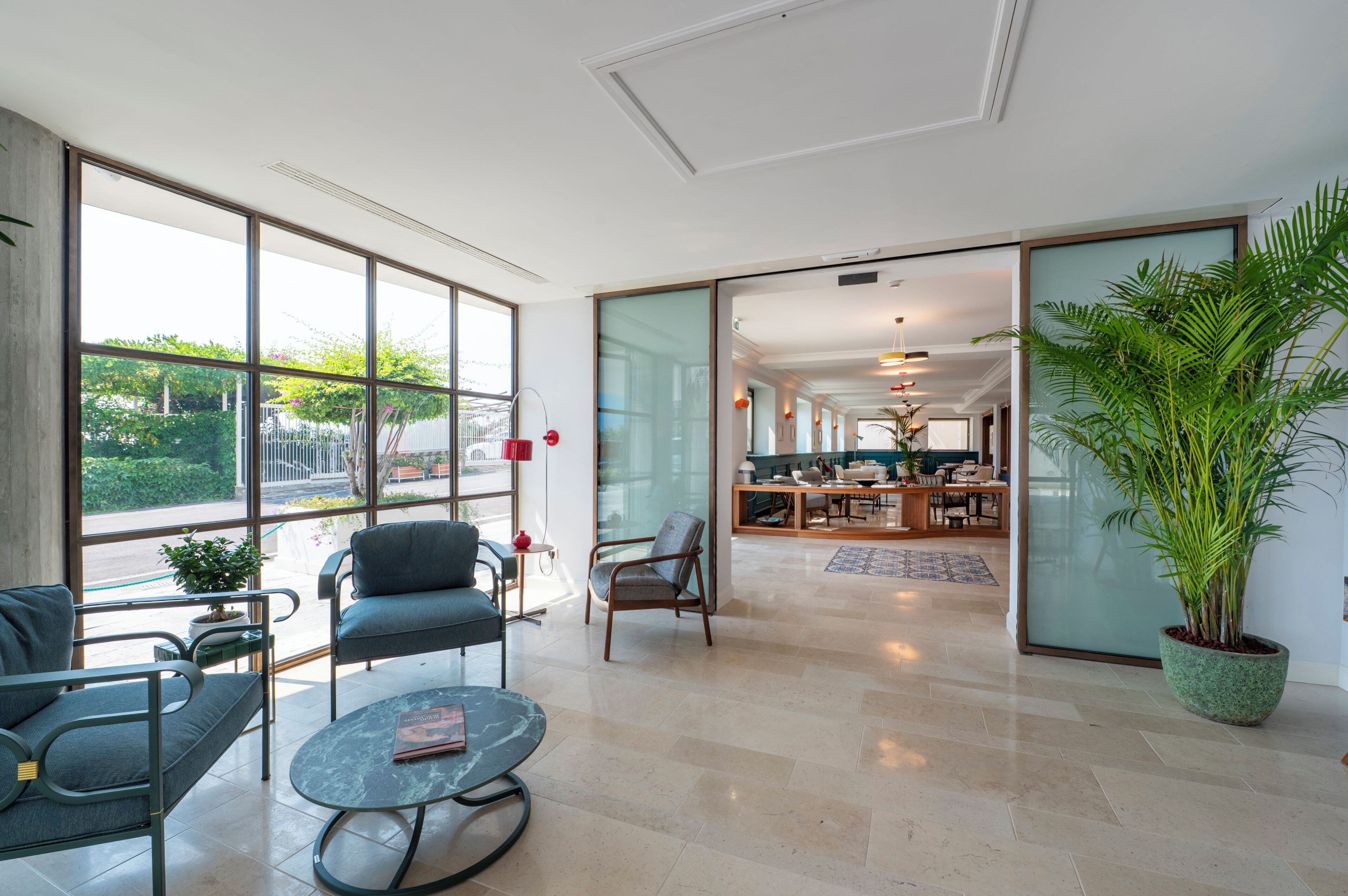 A spacious hotel lobby with a dining area, large windows, and a potted plant.