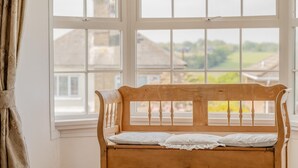 A wooden bench with a white cushion in front of a large window with multiple panes. - 5 Bed in Seaview (oc-n33058) (Seaview)