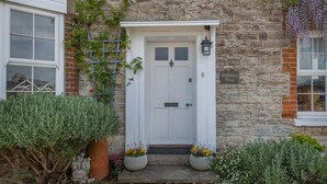 A stone building with a white door, a small porch, and potted plants. - 5 Bed in Seaview (oc-n33058) (Seaview)