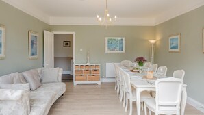 A dining area with a white table set for four, surrounded by white chairs, a chandelier, and a white cabinet with baskets. - 5 Bed in Seaview (oc-n33058) (Seaview)