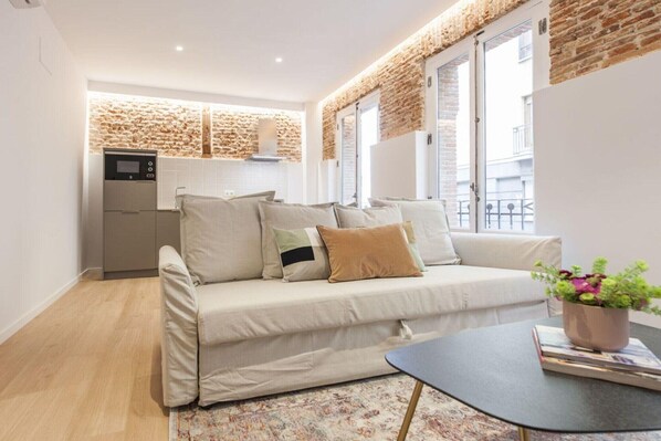 Un espacio habitable compacto con sofá, una mesita, zona de cocina y pared de ladrillo.