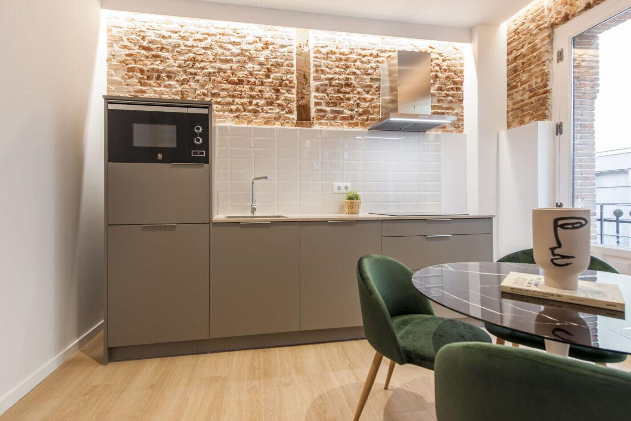 A modern kitchen with a stone backsplash, a built-in oven, and a dining area with a glass table and green chairs.