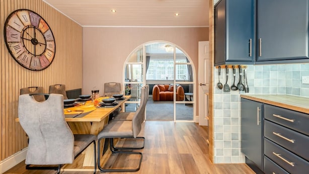 Una cocina moderna con armarios oscuros, una mesa de comedor de madera y un gran reloj de pared.