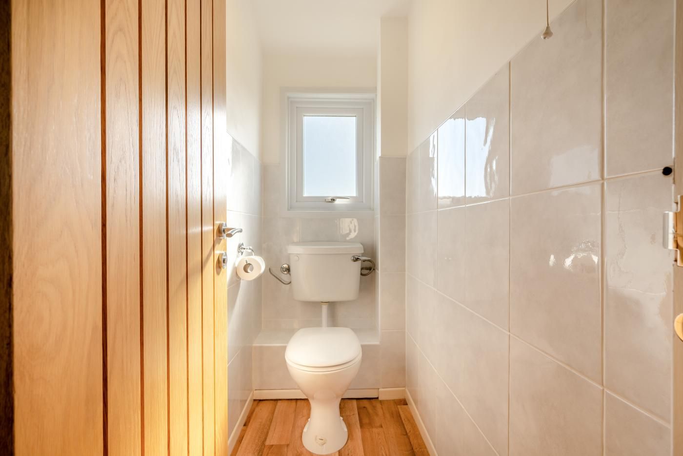 Un bagno piccolo e compatto con il water, una finestra sopra il lavandino e una porta in legno.