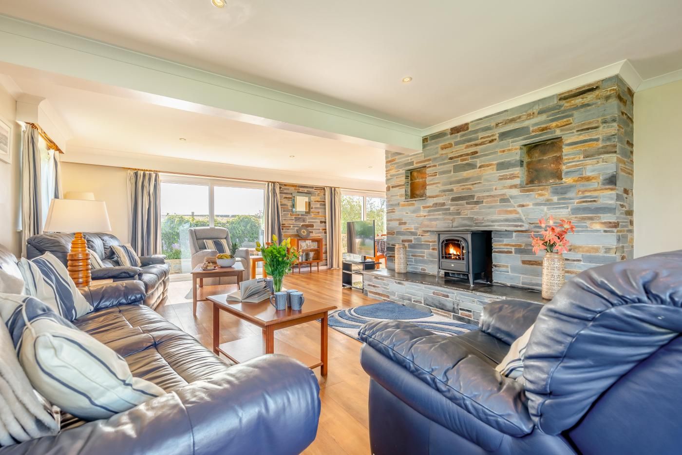 A spacious living room with leather sofas, a stone fireplace, and a large window.