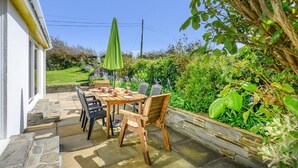 An outdoor patio with a table and chairs, a green umbrella, and a stone pathway leading to a house. - 4 Bed in Harlyn Bay (oc-t35030) (Harlyn Bay)