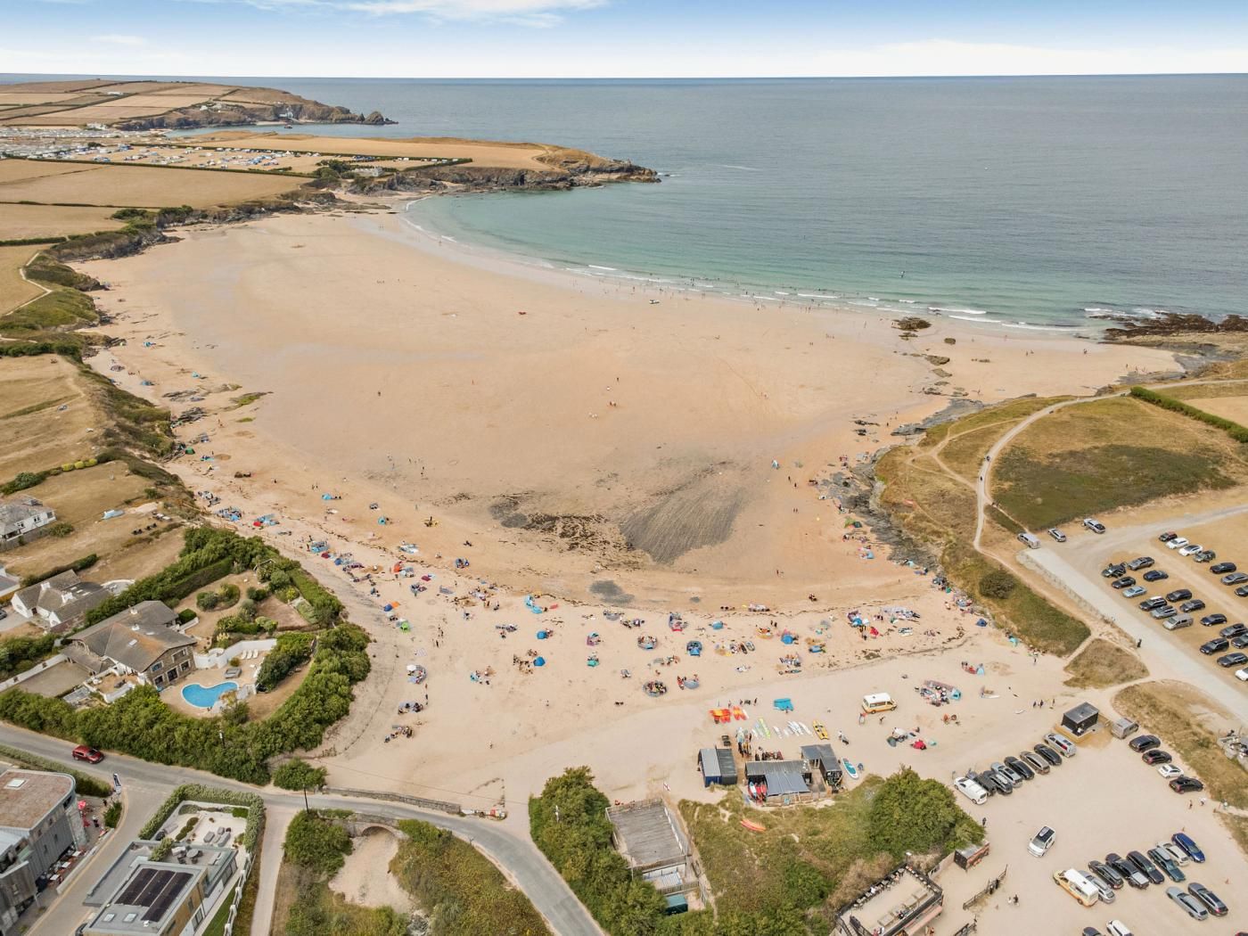 An aerial view of a beach with a parking lot, beach umbrellas, and a swimming pool.