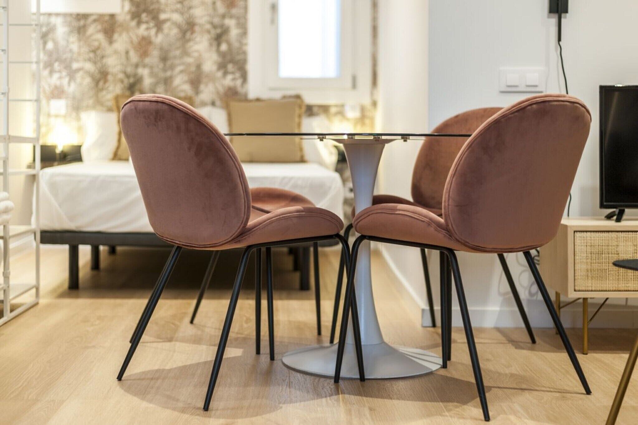 Quarto moderno com cama, mesa com cadeiras, televisão e janela.