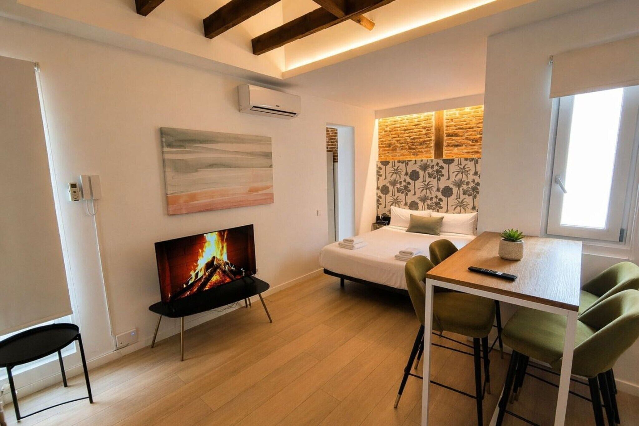 Una habitación compacta con cama, televisión, mesa de comedor con sillas y una mesita con una planta.