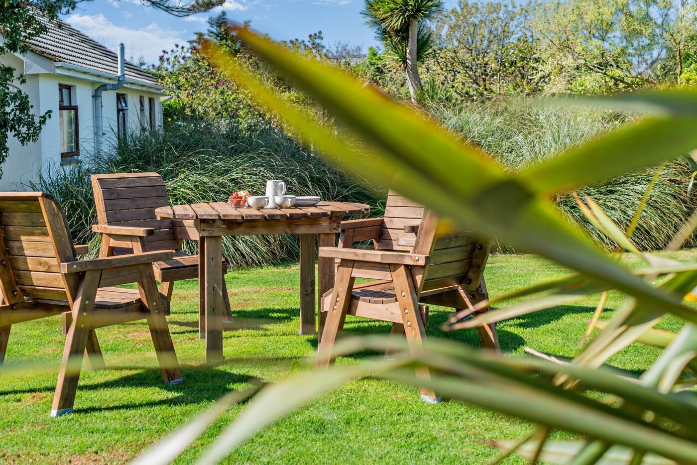 Une table en bois, avec des chaises, et une petite table d’appoint dans un jardin.