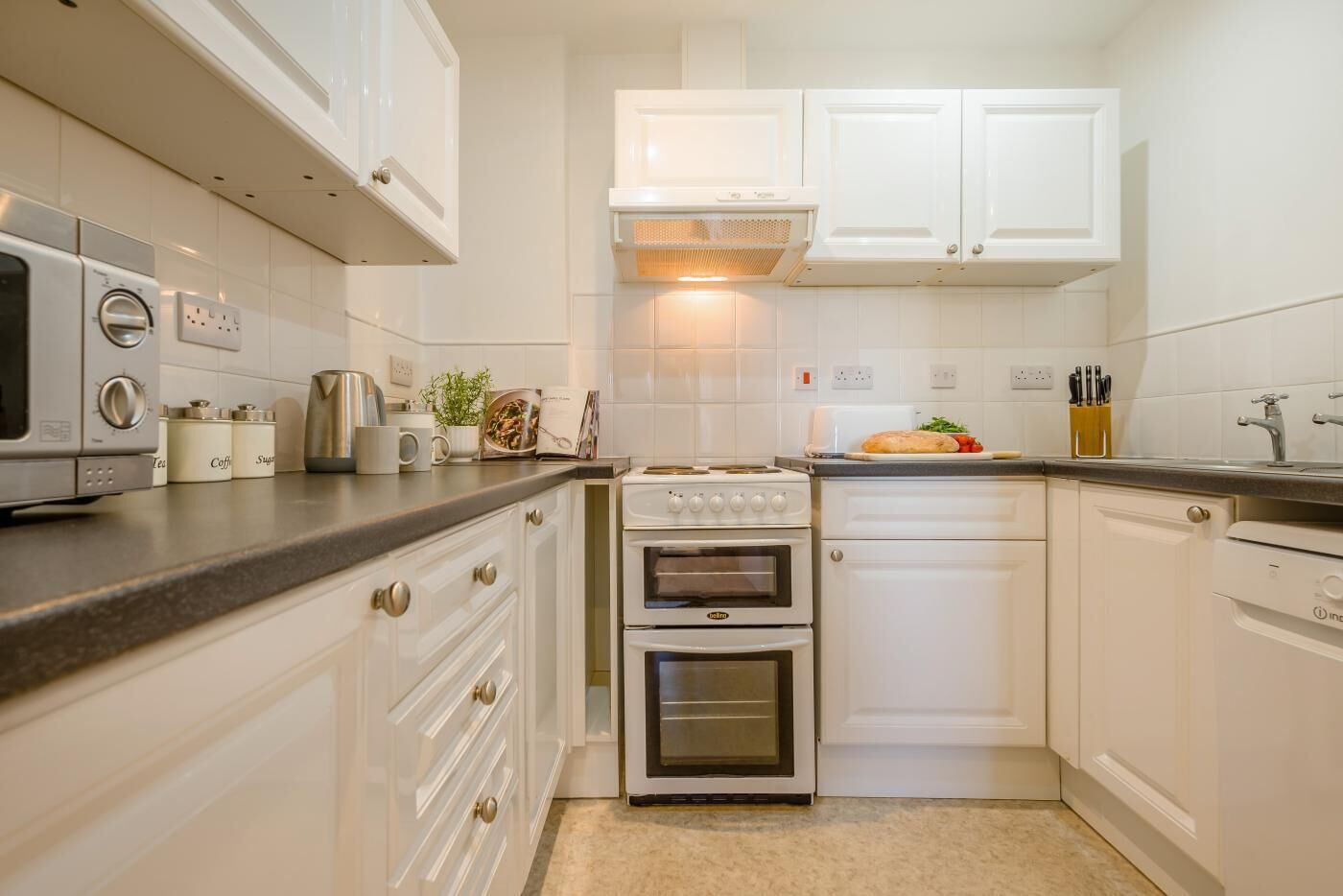 Una cocina compacta con armarios blancos, horno integrado, cafetera y tostadora.