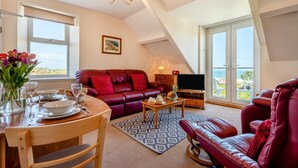 Ein Wohnzimmer mit einem roten Sofa, einem Esstisch, einem Fernseher und Blick auf das Meer.