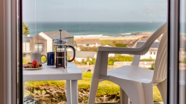 Ein Balkon mit Tisch, French Press, Tasse sowie Teller mit Keksen und Erdbeeren.