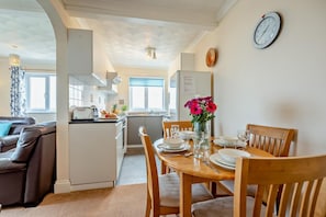 A compact living space with a dining area, kitchenette, and a sofa. - 2 Bed in Harlyn Bay (oc-s35034) (Harlyn Bay)