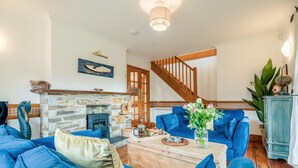 Een woonkamer met een stenen openhaard, blauwe banken, een houten bijzettafeltje en een trap.