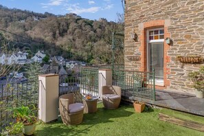 A stone building with a balcony, wicker furniture, and a view of a village. - 2 Bed in Lynmouth (oc-g35037) (Lynmouth)