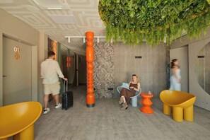 A hotel lobby with a modern design, including a vertical orange column, a seating area with yellow chairs, and a green wall with hanging plants. - Persante Sunrise Collection 6 | Riverview | AC (Kołobrzeg)
