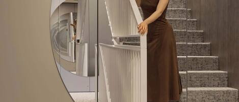 A woman standing on a staircase with a modern design, featuring a circular mirror on the wall.