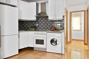 A compact kitchen with white cabinetry, a built-in oven, a washing machine, and a tiled backsplash. - Madrid Hideaway Near Museums (Madrid)