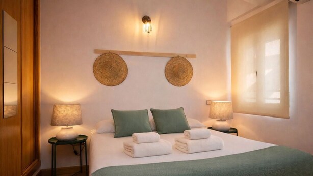 Una cama bien hecha con almohadas verdes, dos lámparas de mesita de noche y una lámpara de pared.