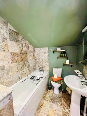 Ein Badezimmer mit Badewanne, Toilette und Waschbecken, mit einer Steinwand und grünen Wänden.