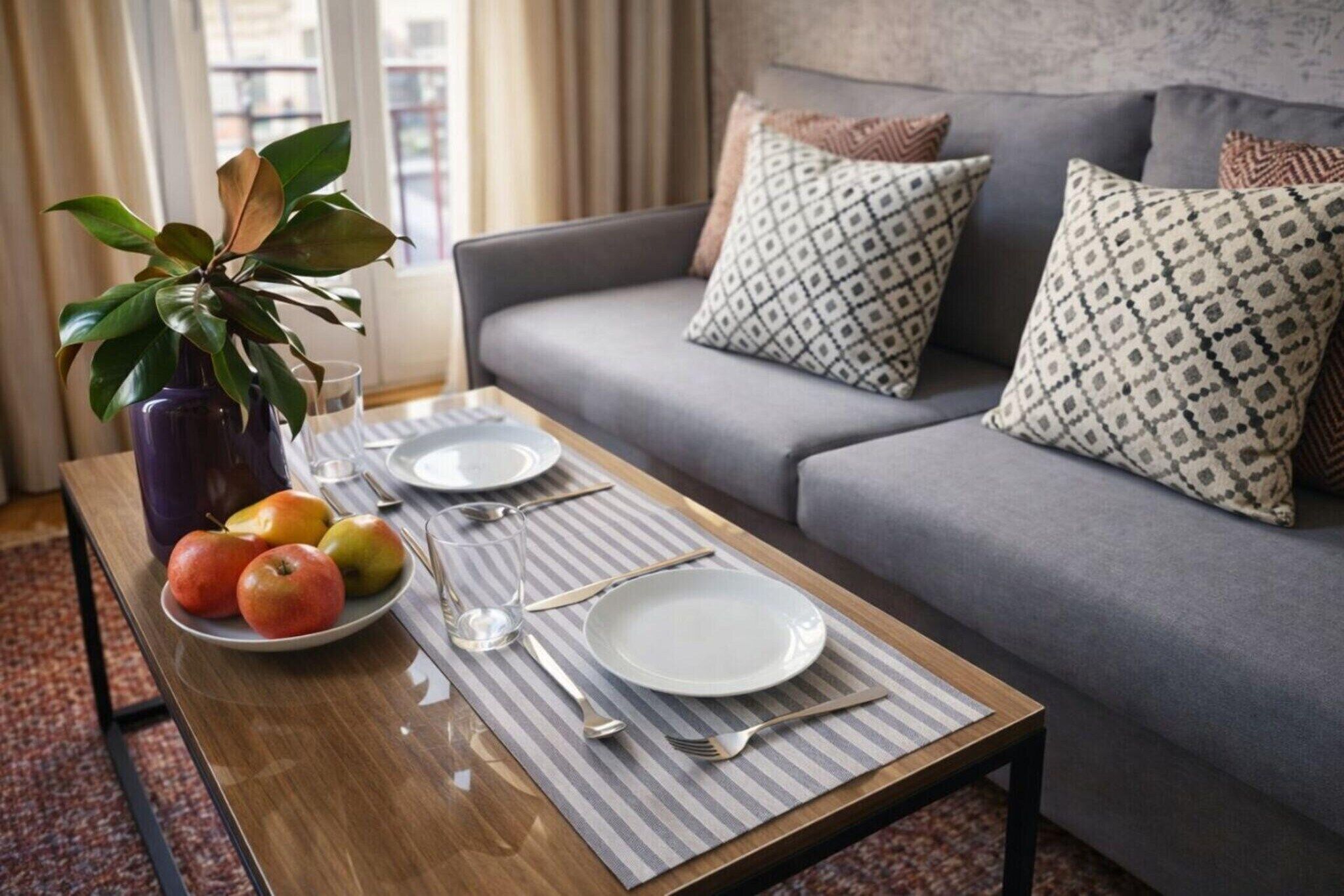 A dining area with a table set for two, a vase with green leaves, and a plate of apples.