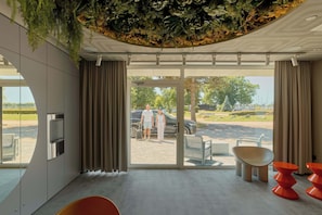 Eine moderne Hotelhalle mit Glastür zum Außenbereich, einem Wasserspender und einer Sitzecke mit orangefarbenen Stühlen.