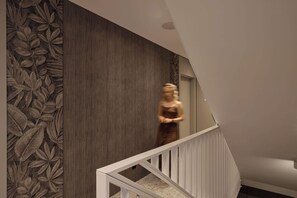 A modern interior with a staircase, a textured wall, and a person walking. - Persante Sunrise Collection 11 | Riverview | AC (Kołobrzeg)