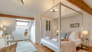 A bedroom with a four-poster bed, a sitting area with a chair and a table, and a window with blinds. - 4 Bed in Appledore (oc-sunni) (Appledore)