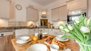 A modern kitchen with white cabinetry, a built-in oven, and a dining area with breakfast items. - 4 Bed in Appledore (oc-sunni) (Appledore)