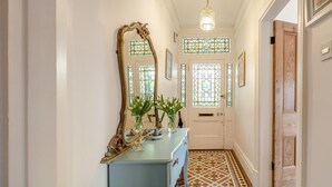 A hallway with a mirror, a blue dresser, a vase with flowers, and a patterned floor. - 4 Bed in Appledore (oc-sunni) (Appledore)