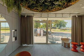Eine moderne Hotelhalle mit Glastür zum Außenbereich, einem Wasserspender und einer Sitzecke mit orangefarbenen Stühlen.