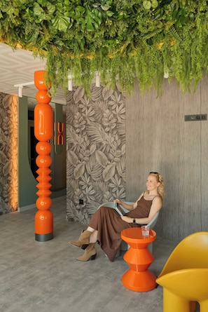A woman seated on a chair in a room with a green wall and a wooden panel. - Persante Sunrise Collection 5 | Riverside | AC (Kołobrzeg)