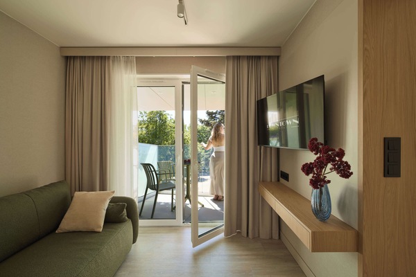 Salon został urządzony w nowoczesnym stylu, łączącym naturalne drewno, jasne beże i oliwkową zieleń. Znajduje się w nim wygodna, rozkładana sofa. Z pomieszczenia można wyjść bezpośrednio na balkon.