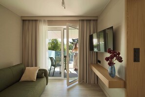 A modern living room with a sofa, a flat-screen TV mounted on a wooden wall, a glass door leading to an outdoor area, and a vase with red flowers on a wooden console. - Persante Sunrise Collection 5 | Riverside | AC (Kołobrzeg)