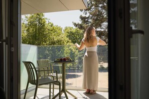 A woman standing on a balcony with a table and chairs, overlooking a garden. - Persante Sunrise Collection 5 | Riverside | AC (Kołobrzeg)