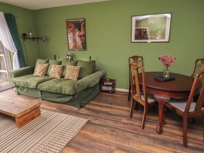 Ein Zimmer mit grünen Wänden, einem Sofa, einem Esstisch mit Stühlen und zwei gerahmten Bildern an der Wand.