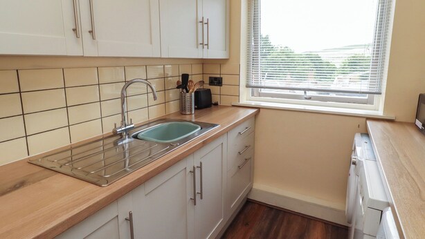 A kitchen with a sink, cabinets, a window with blinds, and a toaster. - Flodden Apartment (Wooler)