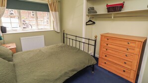 A bedroom with a bed, dresser, and a window with curtains. - Flodden Apartment (Wooler)