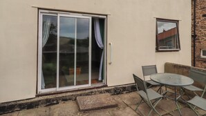 A building with a large sliding glass door, a small window, and a round metal table with chairs. - Flodden Apartment (Wooler)