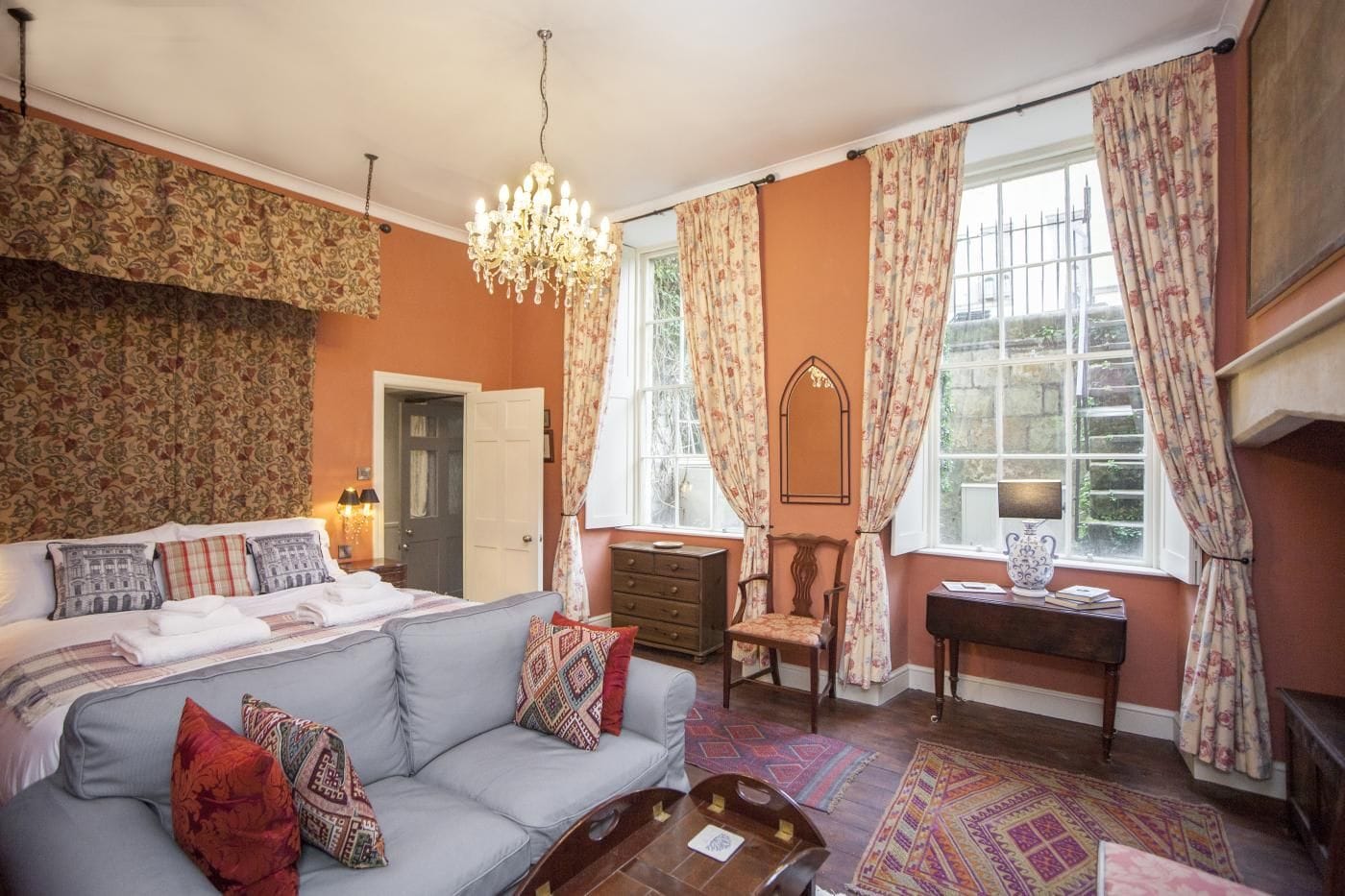 A cozy living room with a sofa, a coffee table, a fireplace, and a large window with curtains.