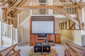A spacious room with a brick fireplace, a large screen for viewing, and a staircase with exposed wooden beams. - 6 Bed in Ardleigh (oc-b35089) (Ardleigh)