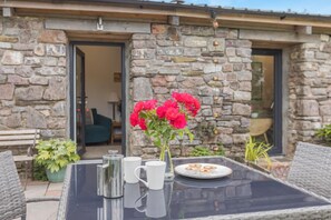 Un bâtiment en pierre avec une porte en verre, une table sur laquelle se trouve un vase de fleurs et une assiette de pâtisseries.