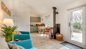 Ein gemütliches Wohnzimmer mit einem türkisblauen Sofa, ein Essbereich mit Holzsesseln, eine Küche mit grünen Schränken und ein großes Fenster.